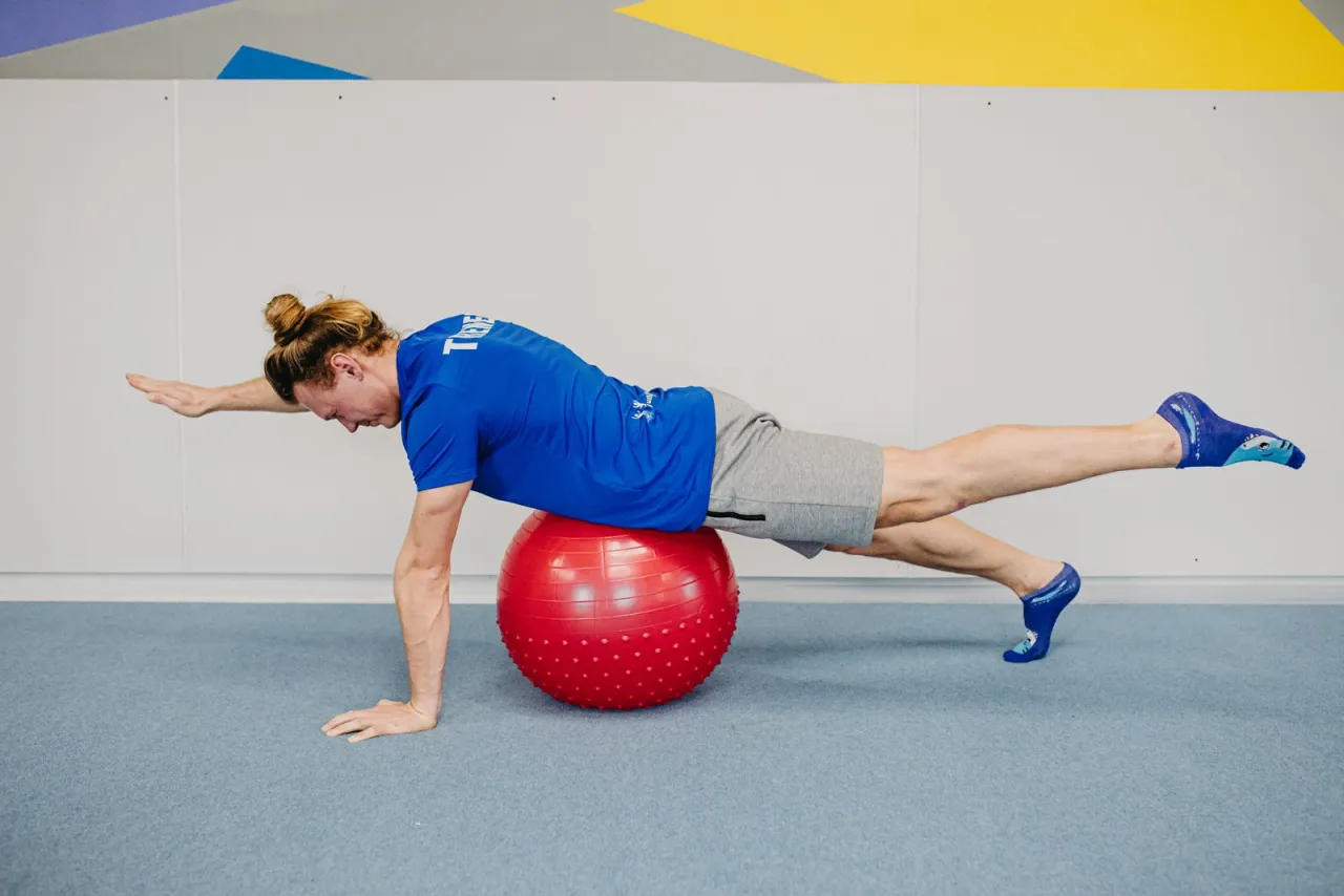 Mężczyzna wykonuje ćwiczenie na piłce gimnastycznej, kt&oacute;re pomaga w odchudzaniu. Wzmacnia mięśnie brzucha i plec&oacute;w.