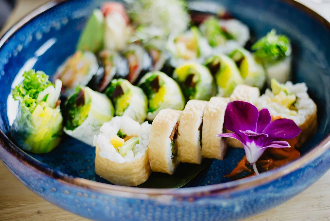 Kolorowe rolki sushi, idealne jako sushi dla dzieci, podane na niebieskiej talerzu z fioletowym kwiatem.