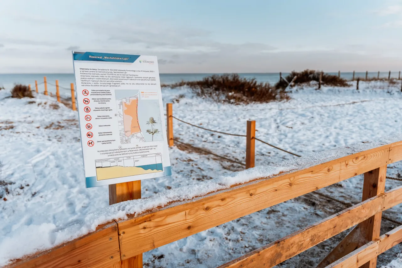 Tablica informacyjna w rezerwacie przyrody Mechelińskie Łąki, zimowy krajobraz nad morzem.