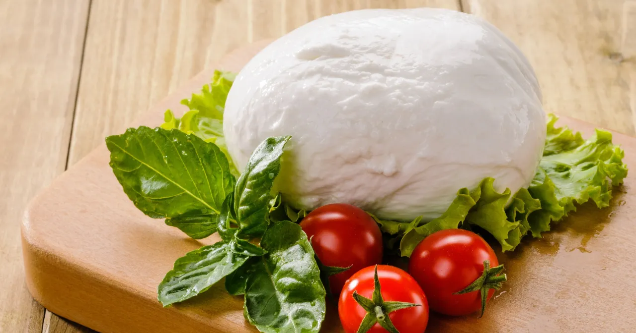 Świeża mozzarella, pomidorki i bazylia na desce. Dowiedz się, ile tłuszczu ma mozzarella, by cieszyć się jej smakiem.