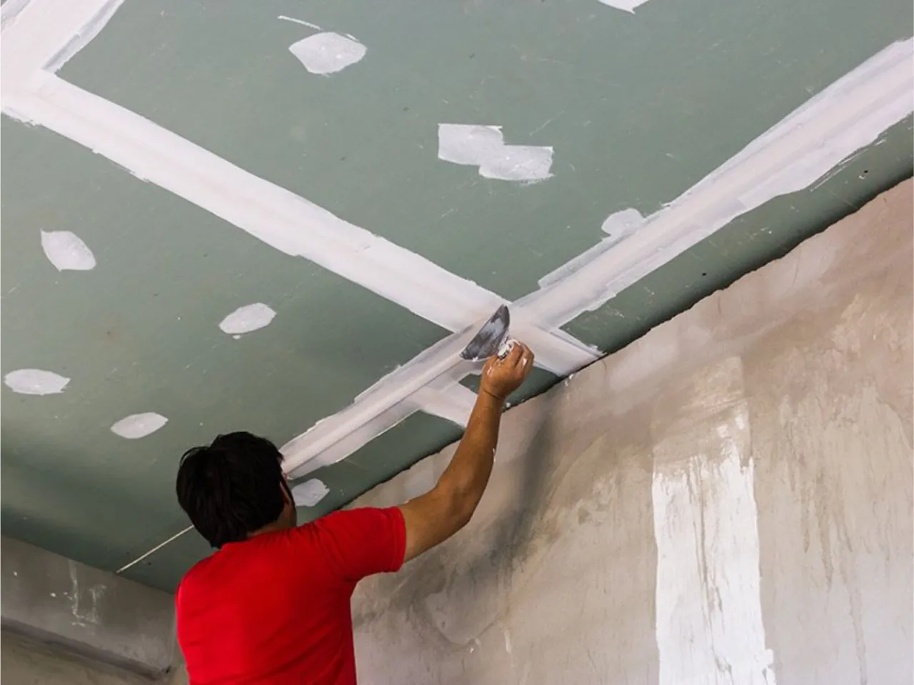 Pracownik nakłada gładź na płyty gipsowe na suficie, przygotowując je do malowania.