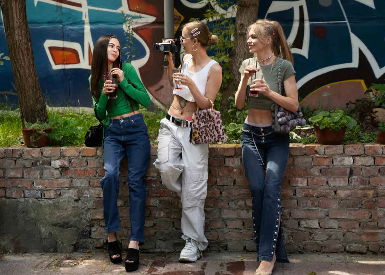 Trzy dziewczyny w boj&oacute;wkach i crop topach pozują przy murze z graffiti. Jedna z nich trzyma aparat. Jakie buty do boj&oacute;wek?