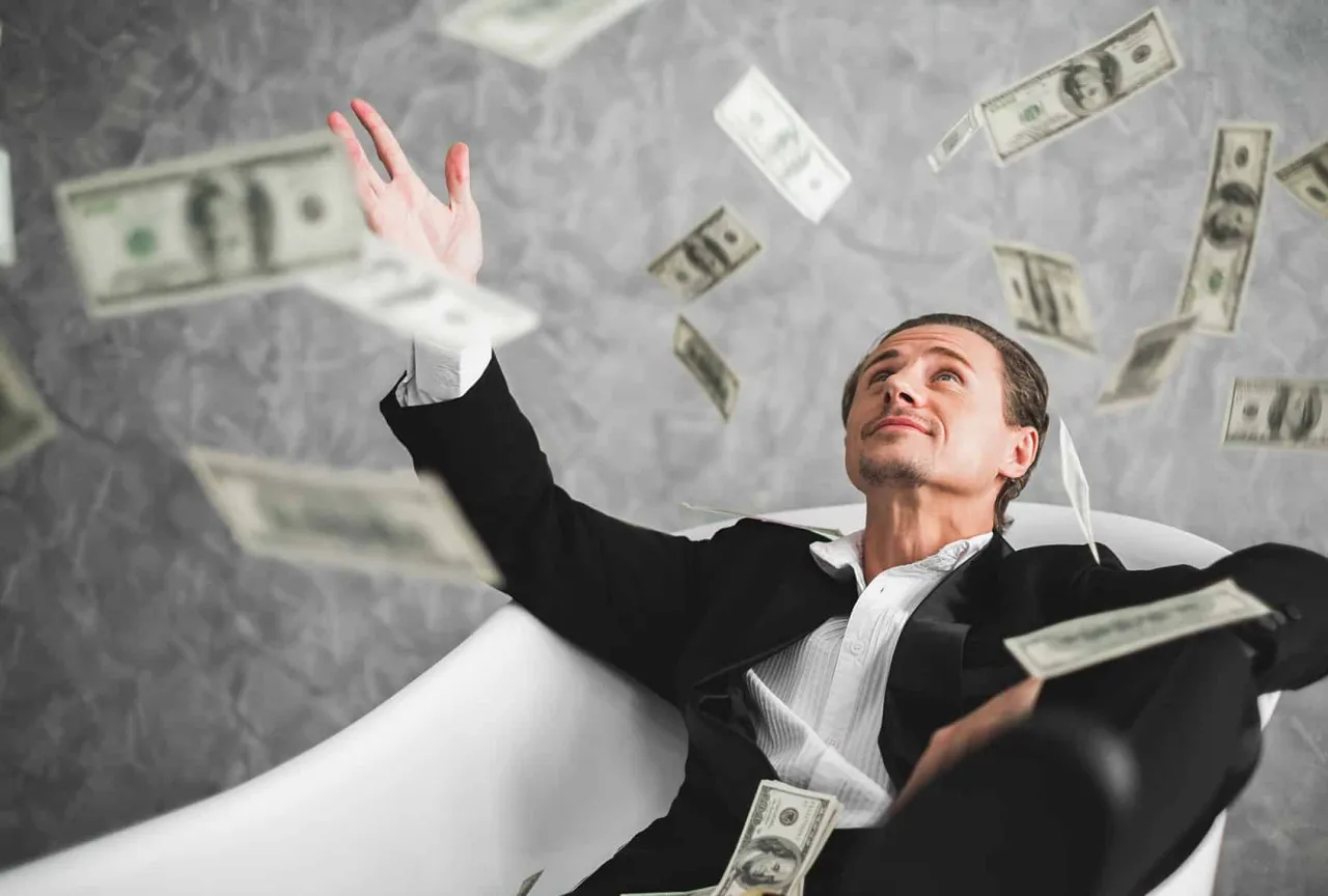 Mężczyzna w wannie rzuca banknotami, zastanawiając się, czy dobra materialne czynią człowieka szczęśliwym.