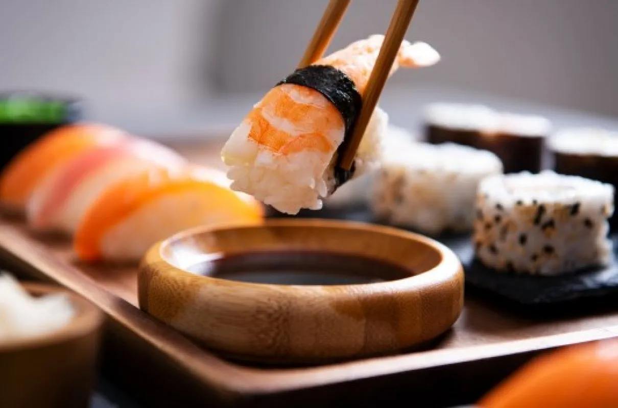 Paleczkami podnoszony do sosu krewetkowy handroll sushi. Obok łosoś i inne rolki.