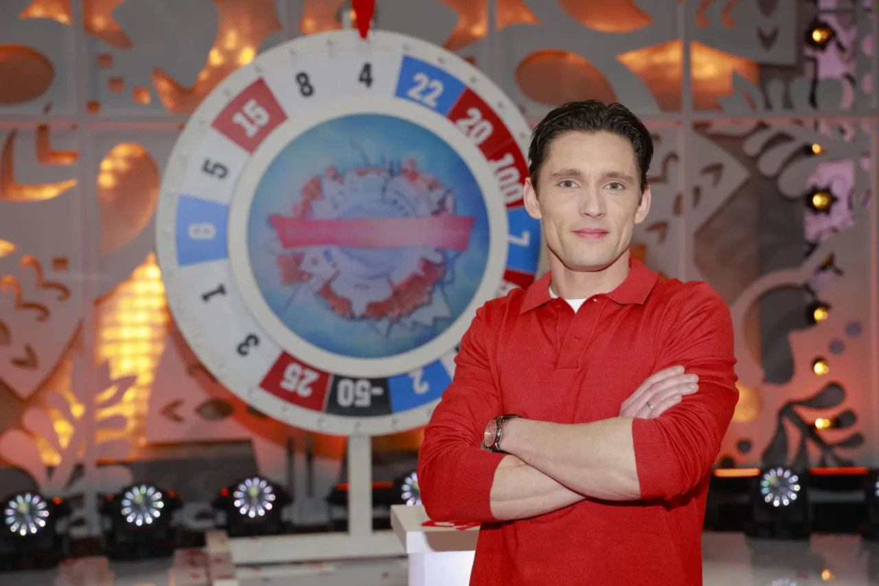 Filip Gurłacz w czerwonej koszulce z kołem fortuny w tle, jak w programie 