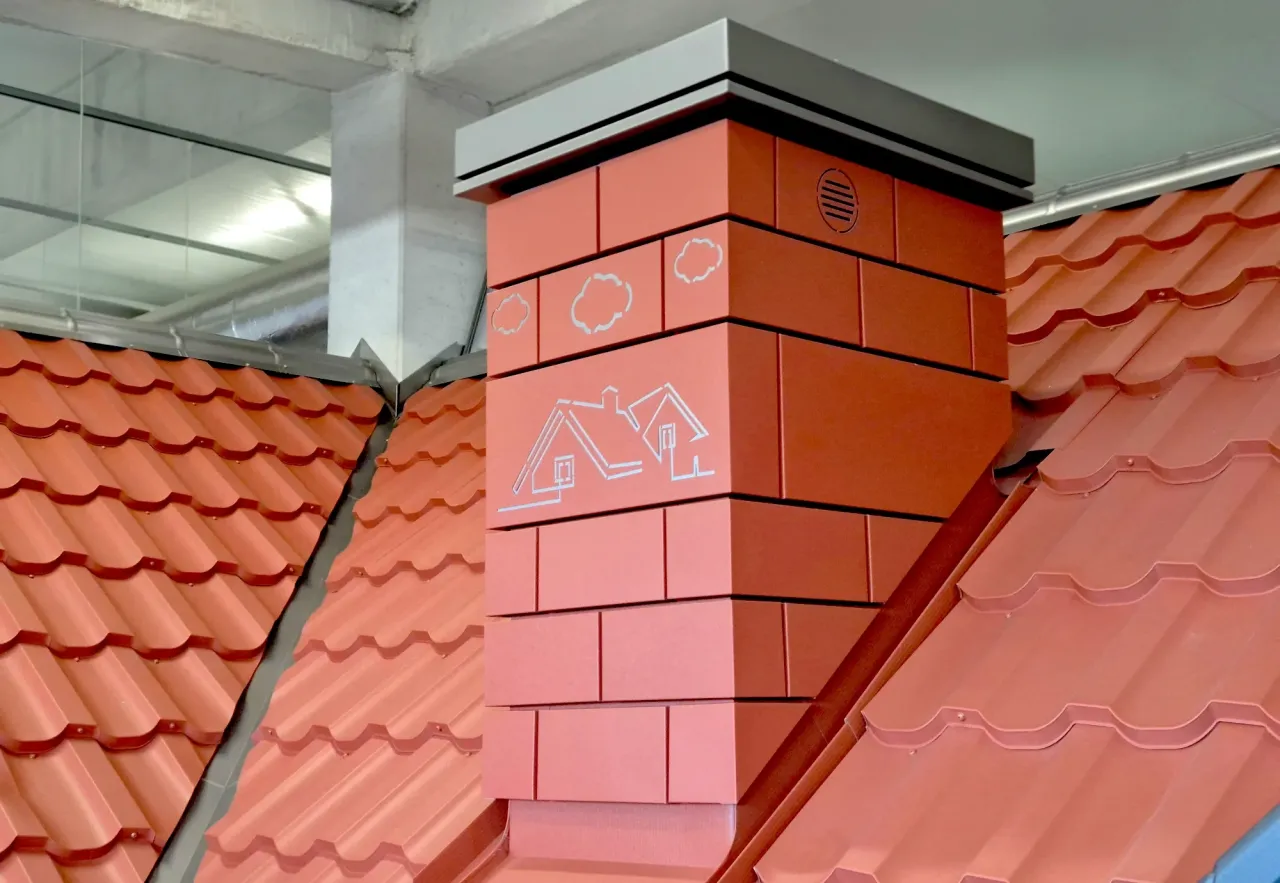 Nowoczesny spos&oacute;b, jak obudować komin wewnątrz domu. Czerwony komin z białymi zdobieniami w kształcie chmurek i domk&oacute;w.