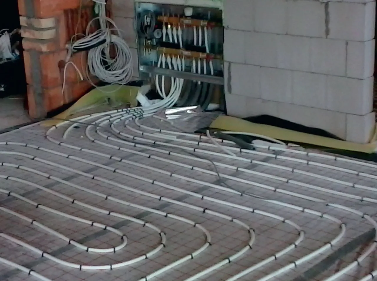 Instalacja ogrzewania podłogowego. Zastanawiasz się, ile kosztuje ogrzewanie podłogowe? Widok rur grzewczych i rozdzielacza.