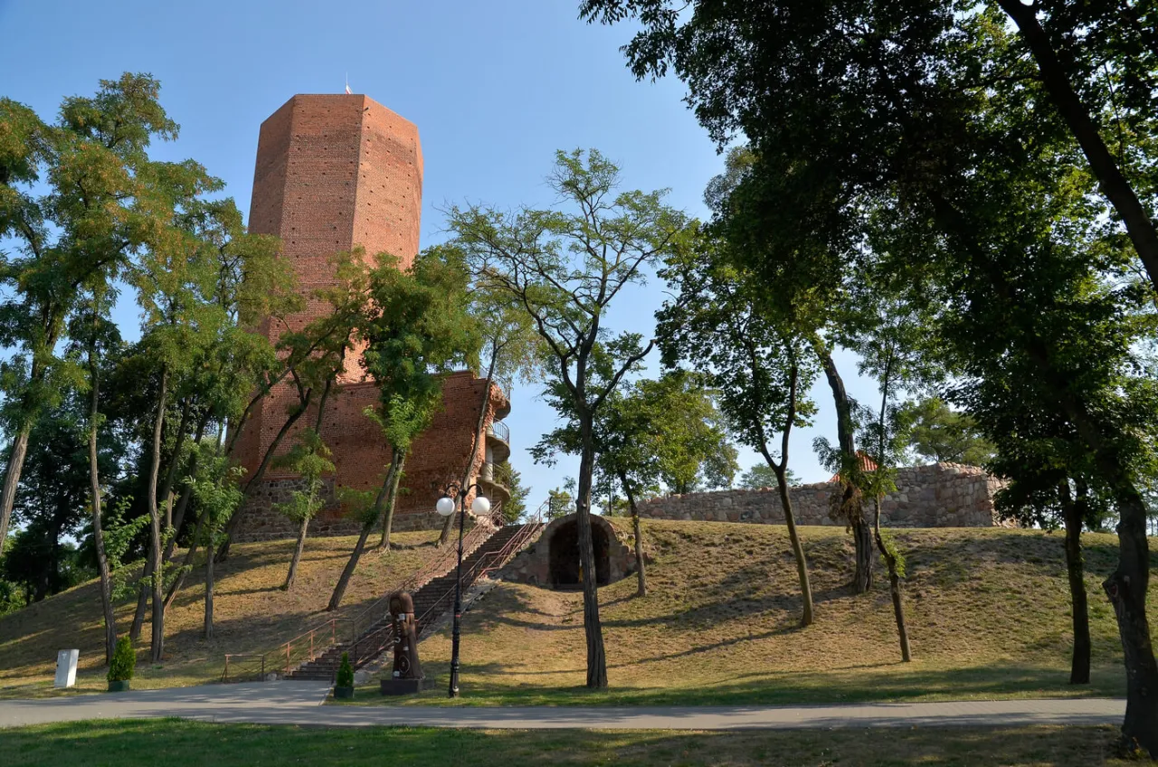 Ceglana wieża, niczym z legendy o mysiej wieży, wznosi się na wzg&oacute;rzu wśr&oacute;d drzew.