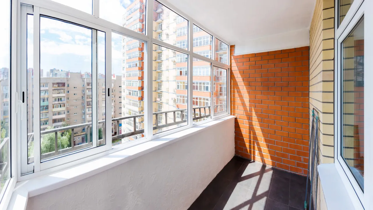 Zabudowany taras z widokiem na miejską zabudowę. Jasne okna i ceglana ściana tworzą przytulne wnętrze.