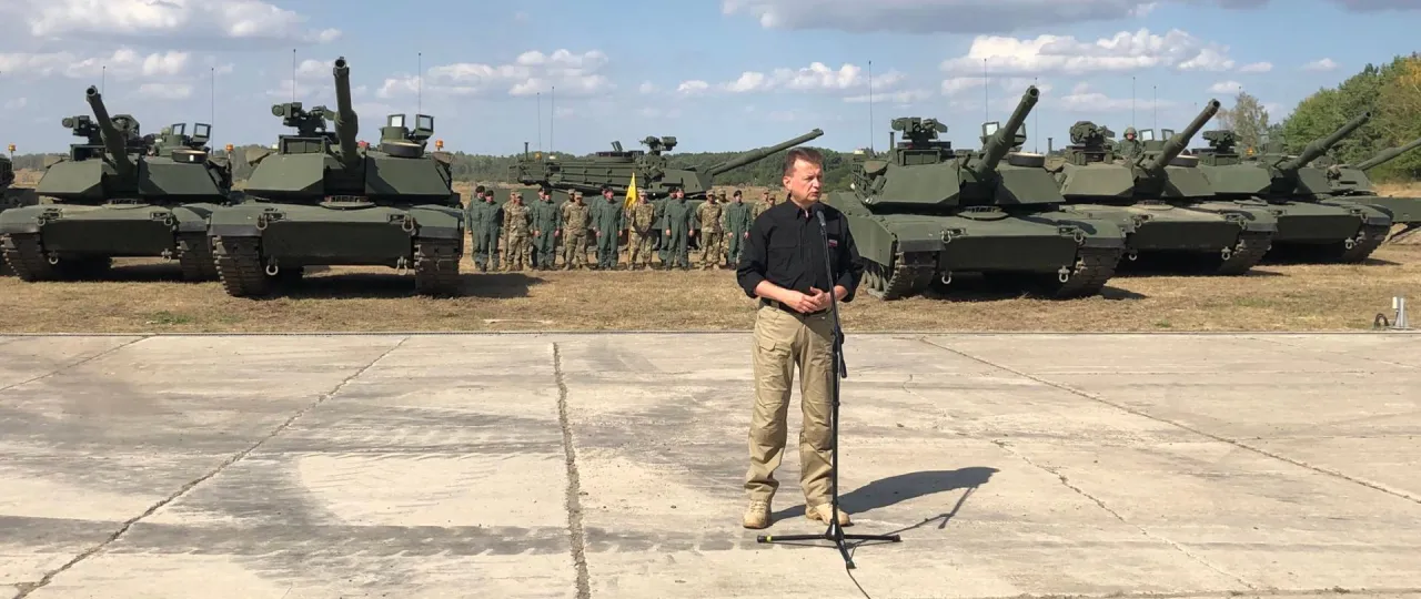 Mężczyzna przemawia przed rzędem czołg&oacute;w, być może wyjaśniając, jak zostać kierowcą czołgu.