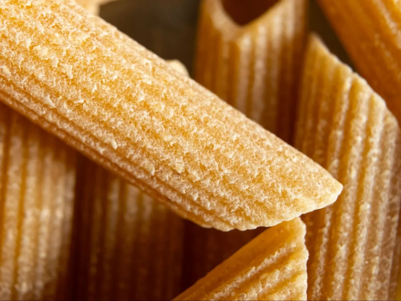 Zbliżenie na makaron pełnoziarnisty vs zwykły. Widać jego chropowatą teksturę i lekko brązowy kolor.