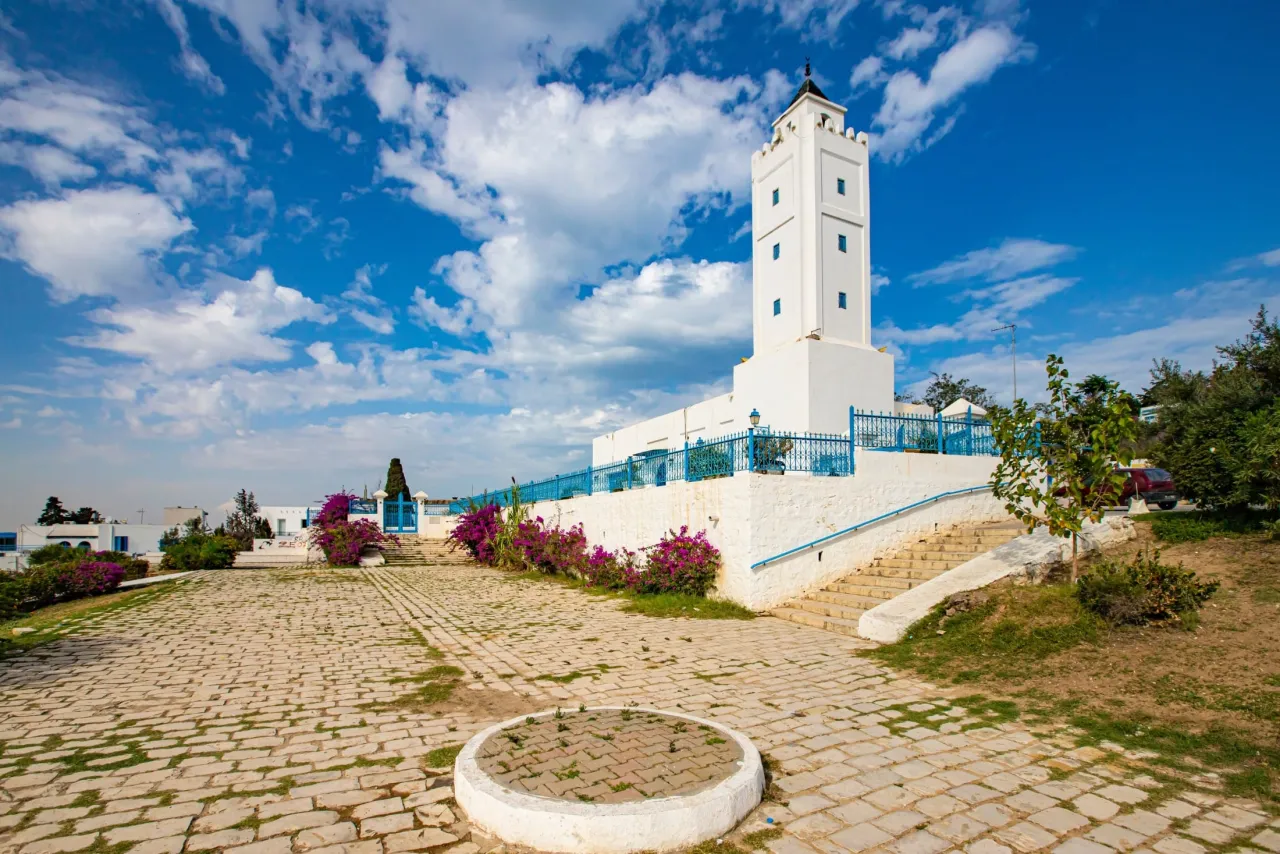Biały meczet z niebieskimi okiennicami i ogrodzeniem, otoczony bujną zielenią i kwitnącymi krzewami. To jedno z tunezyjskich najpiękniejszych miejsc.
