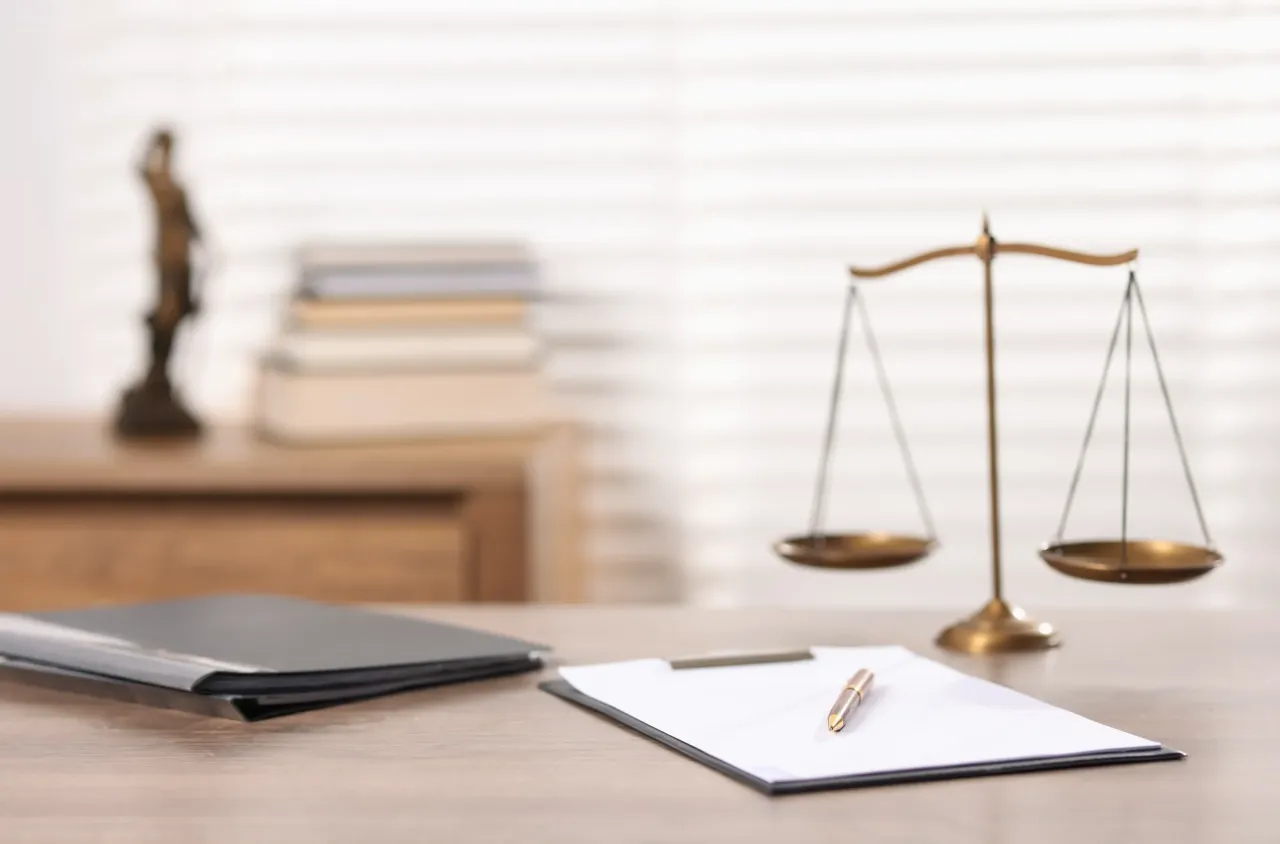 Na stole prawniczym leżą dokumenty, pióro i waga sprawiedliwości. To miejsce, gdzie przygotowuje się rozprawę o alimenty, co mówić, by uzyskać sprawiedliwy wyrok.