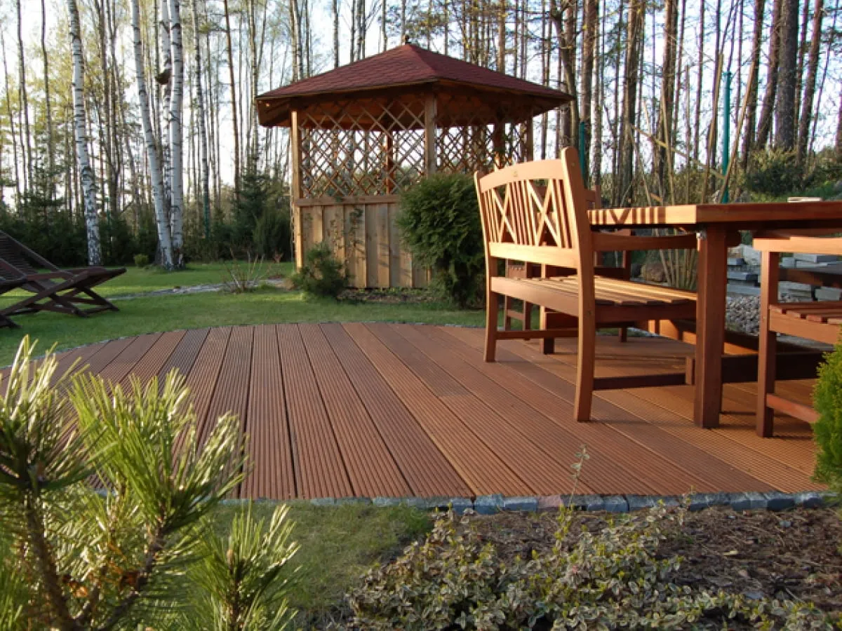 Drewniany taras na trawie, idealne miejsce na relaks. W tle altana i meble ogrodowe.