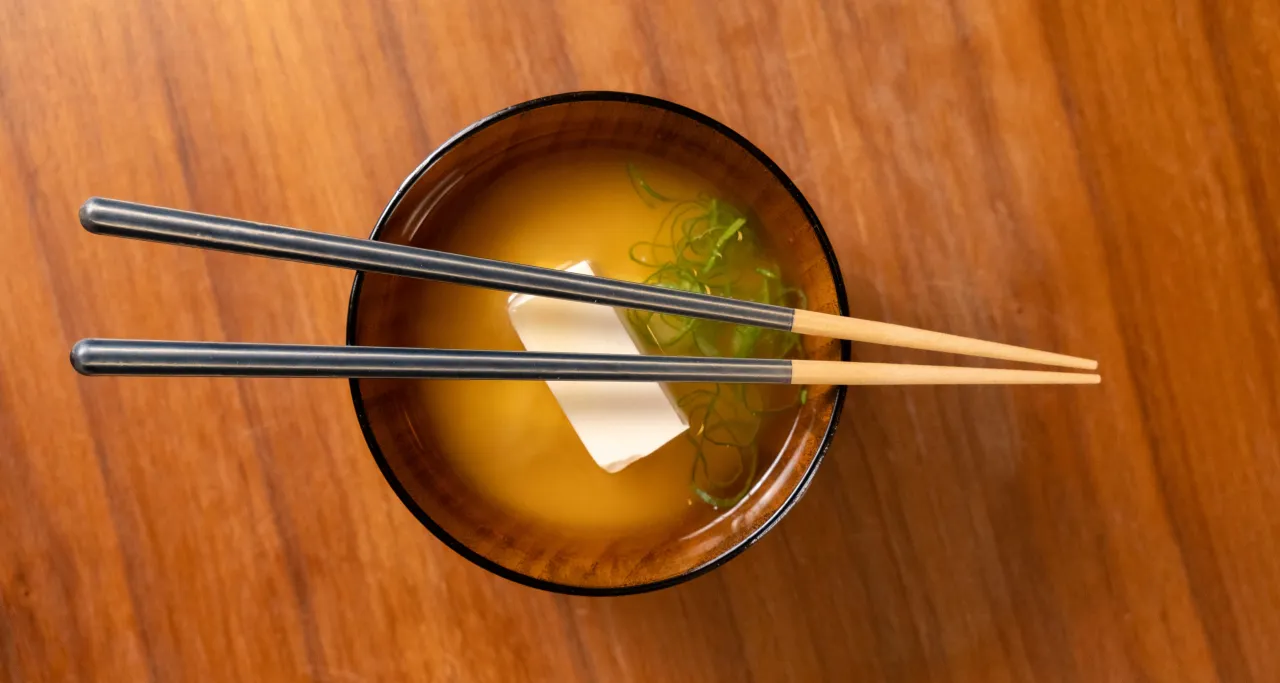 Miseczka z zupą miso i tofu, nad kt&oacute;rą spoczywają pałeczki. Idealny moment na naukę jedzenia pałeczkami.