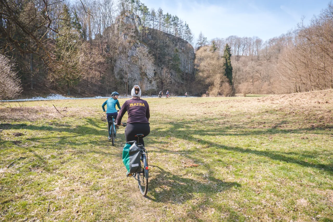 Rowerzyści przemierzają malowniczą trasę rowerową w Ojcowie, podziwiając skalne ściany i wiosenną zieleń.