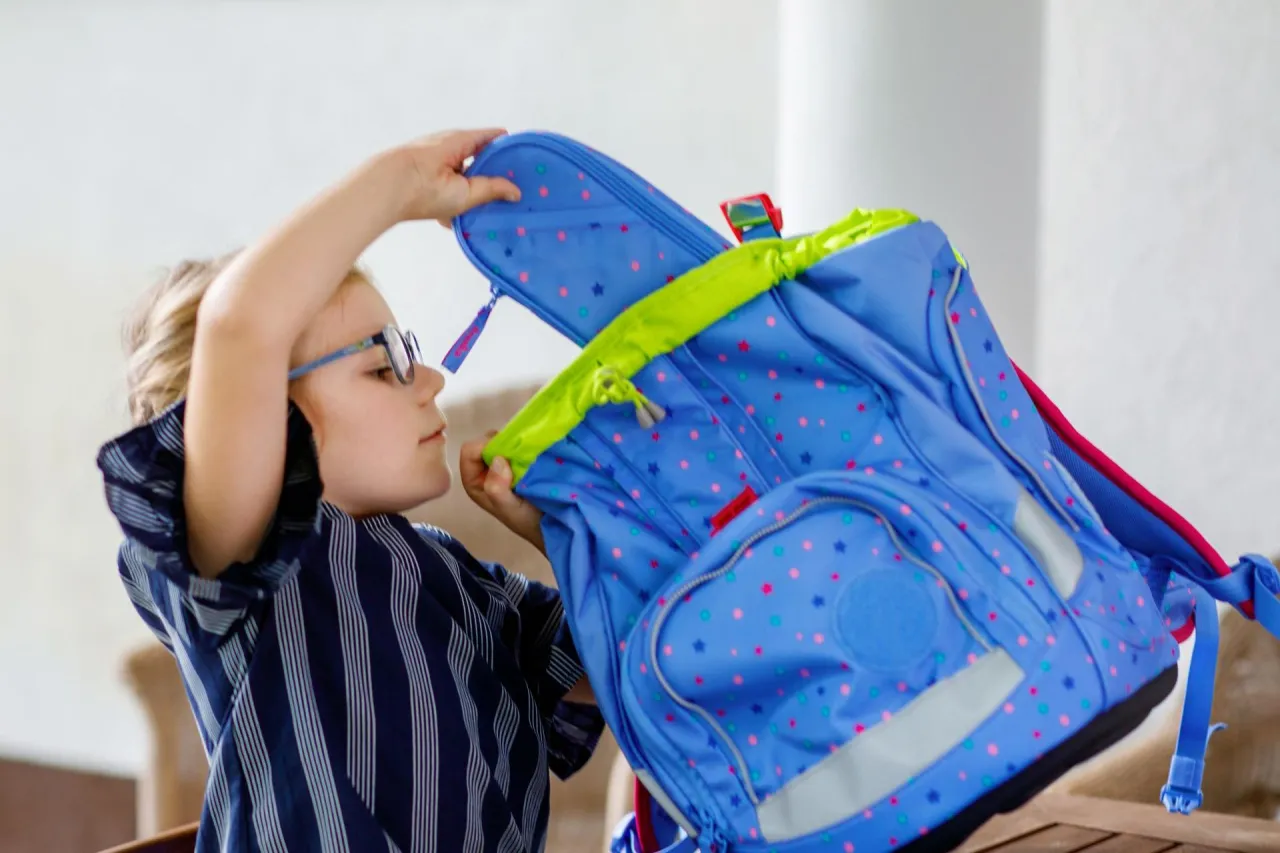 Dziecko z okularami pakuje niebieski plecak w gwiazdki. Zastanawiasz się, ile powinien ważyć plecak do szkoły?