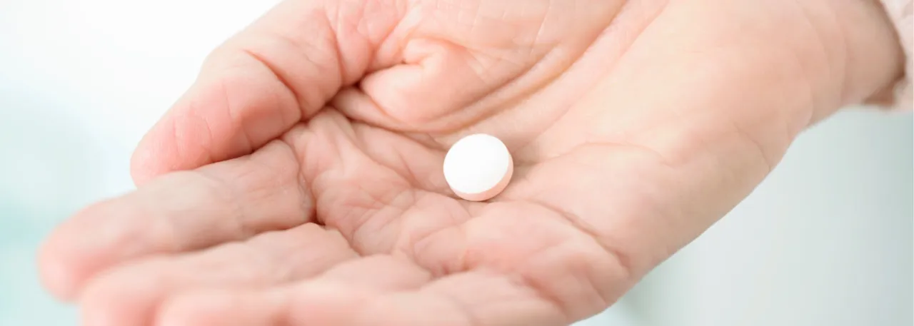 B&oacute;l brzucha? Czy apap pomoże? Jedna biała tabletka spoczywa na dłoni, czekając na rozwiązanie.