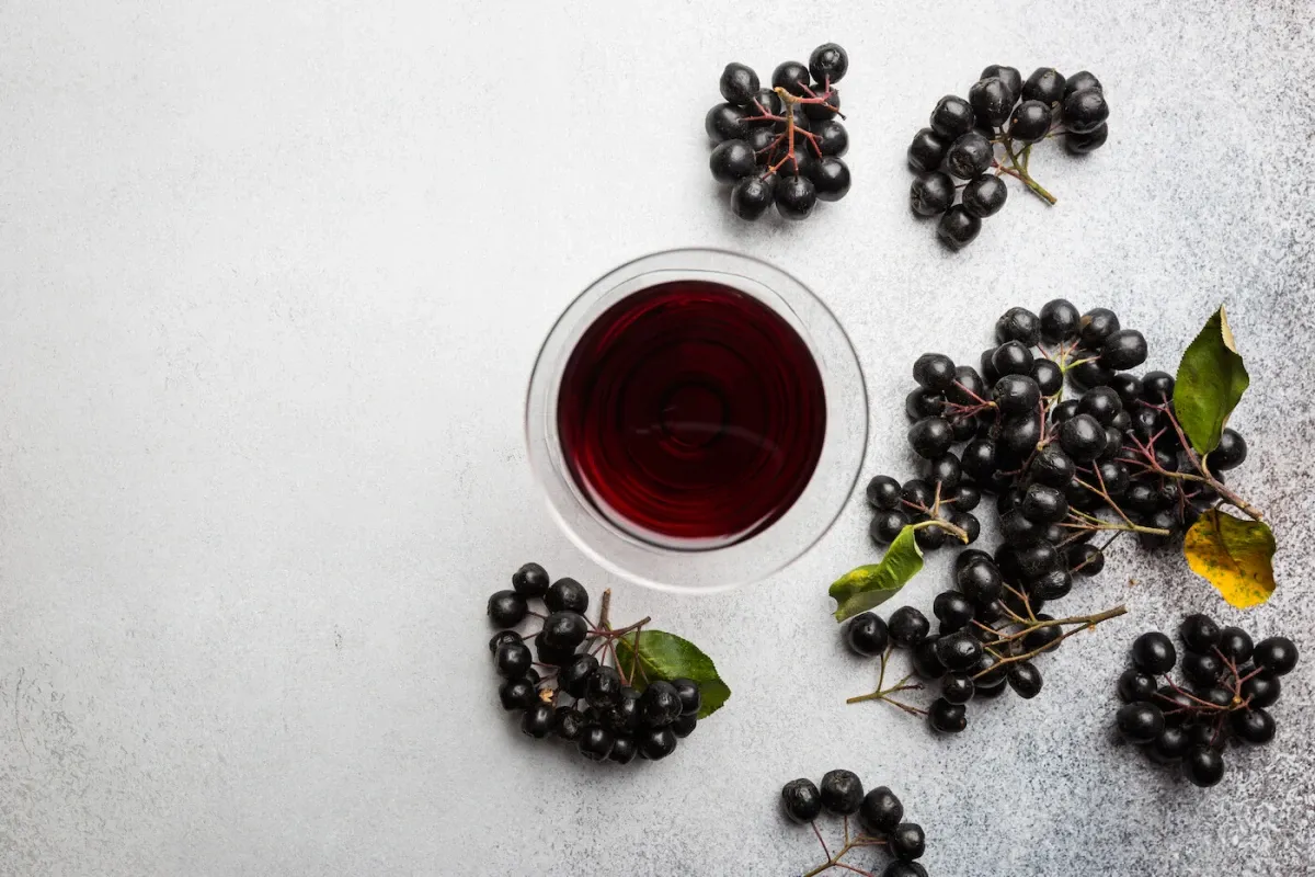 Szklanka z ciemnym sokiem z aronii i kiście świeżych owoc&oacute;w. Idealne do mrożenia aronii na zimę.