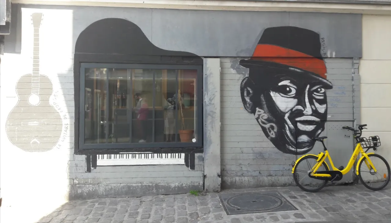 Muzyczna ściana w 13 dzielnicy Paryża: gitara, fortepian i portret mężczyzny w kapeluszu. Obok żółty rower.