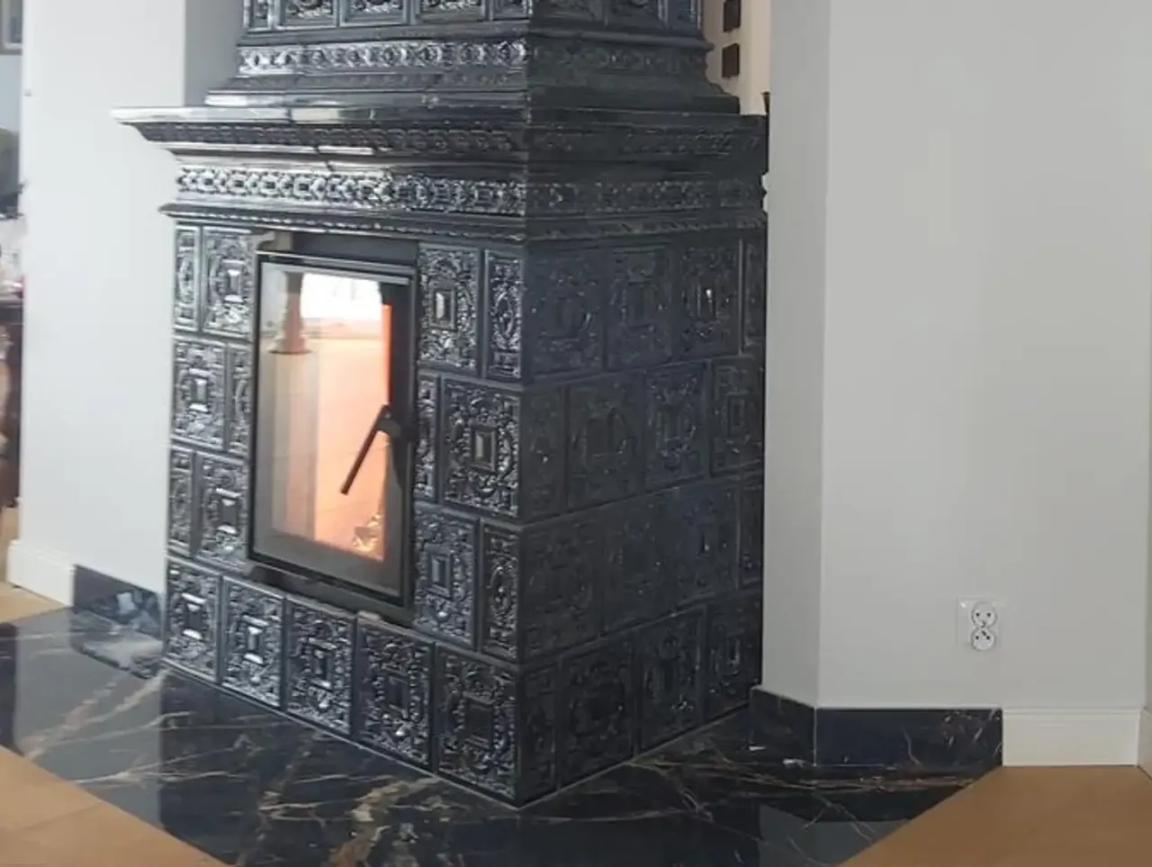 Elegancki, czarny piec kaflowy z przeszklonym paleniskiem zajmuje sporo miejsca, tworząc przytulną atmosferę.