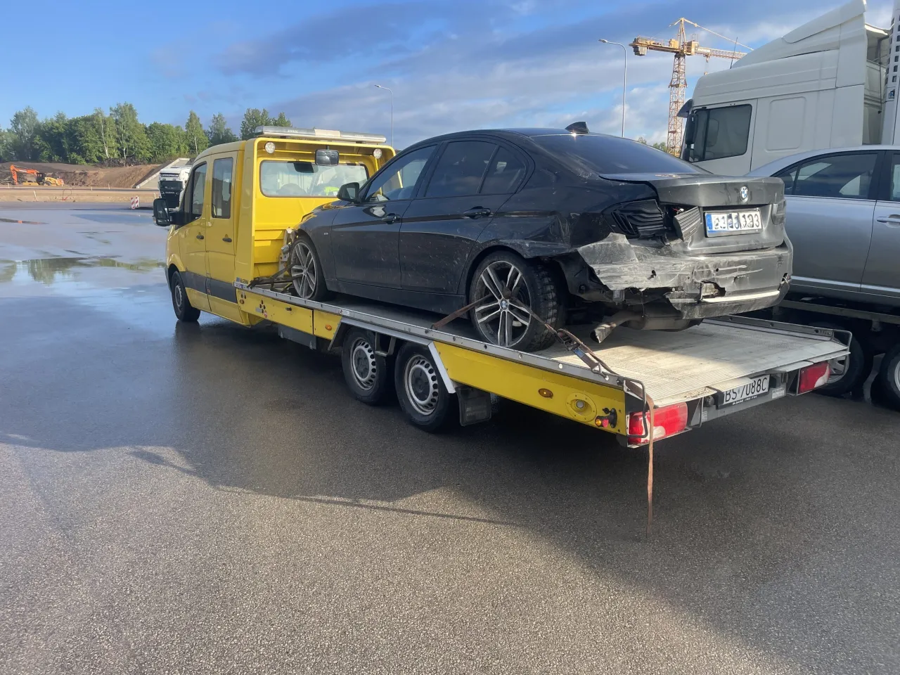 Uszkodzony czarny BMW na żółtej lawecie. Czy można holować samochód na drodze ekspresowej? Tak, jeśli jest to laweta.