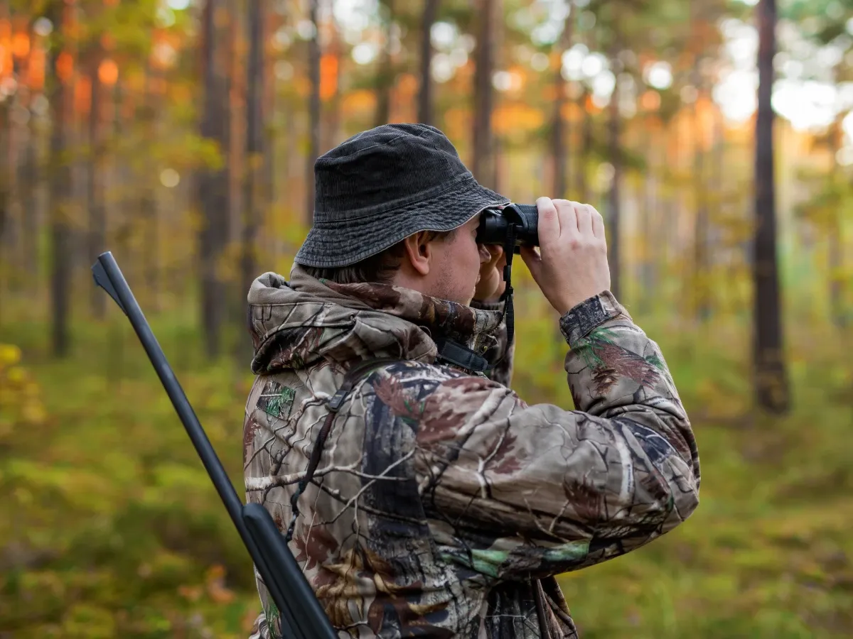 Myśliwy w leśnej głuszy, w jesiennej szacie kamuflażu, przez lornetkę wypatruje zwierzyny. Co myśliwi robią w lesie? Czekają cierpliwie.