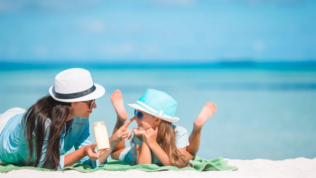 Mama smaruje córkę kremem na plaży. Idealne wakacje w hotelu dla dzieci nad morzem.