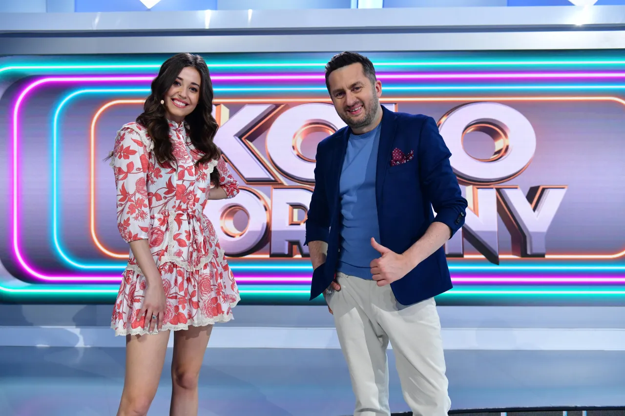 Iza z Koła Fortuny uśmiecha się na tle neonowego logo. Ciekawe, ile zarabia za tę pracę!