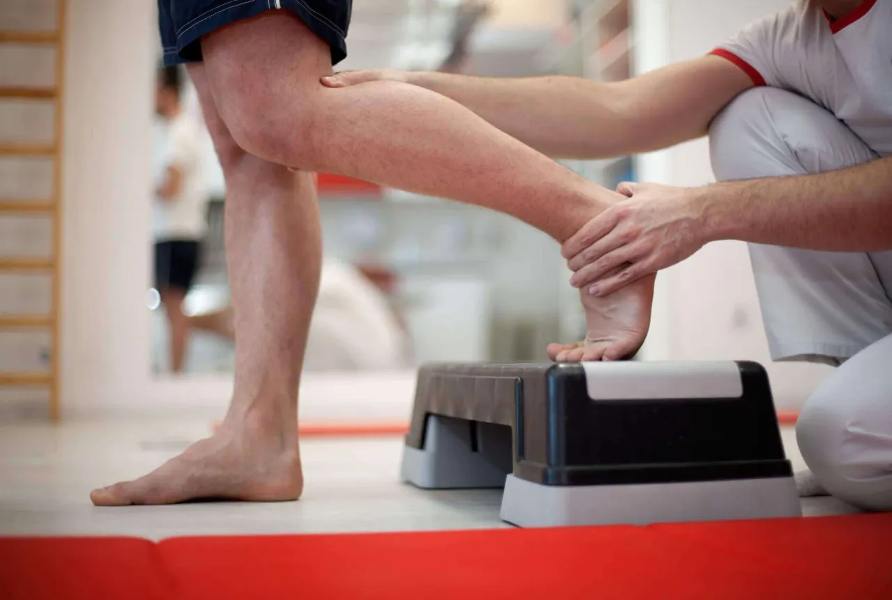 Fizjoterapeuta pomaga pacjentowi ćwiczyć stopę na stopniu, co jest pomocne w rehabilitacji po skręceniu kostki.