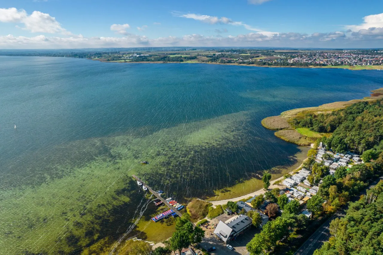Widok na turkusową wodę, zatoczkę z pomostem i ł&oacute;dkami, kemping i las. To najpiękniejsze miejsce na P&oacute;łwyspie Helskim.