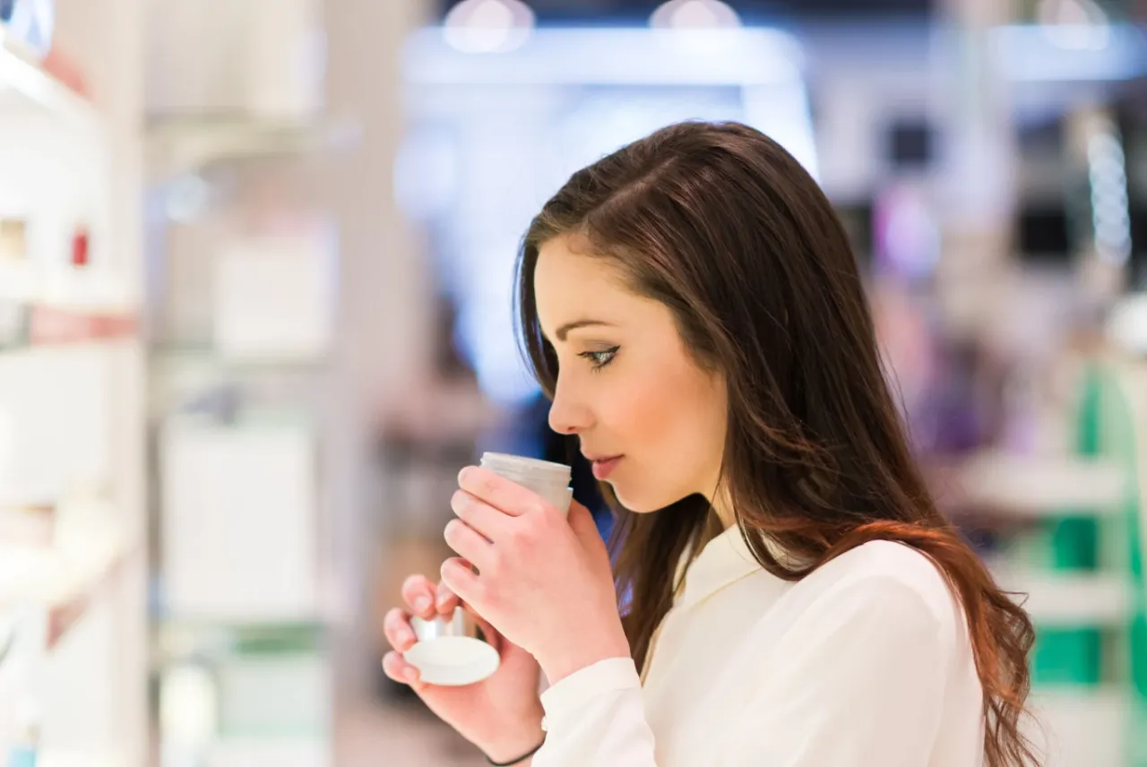 Kobieta wącha perfumy w sklepie. Zastanawia się, gdzie kupić wodę toaletową Basia, by odkryć sw&oacute;j nowy ulubiony zapach.