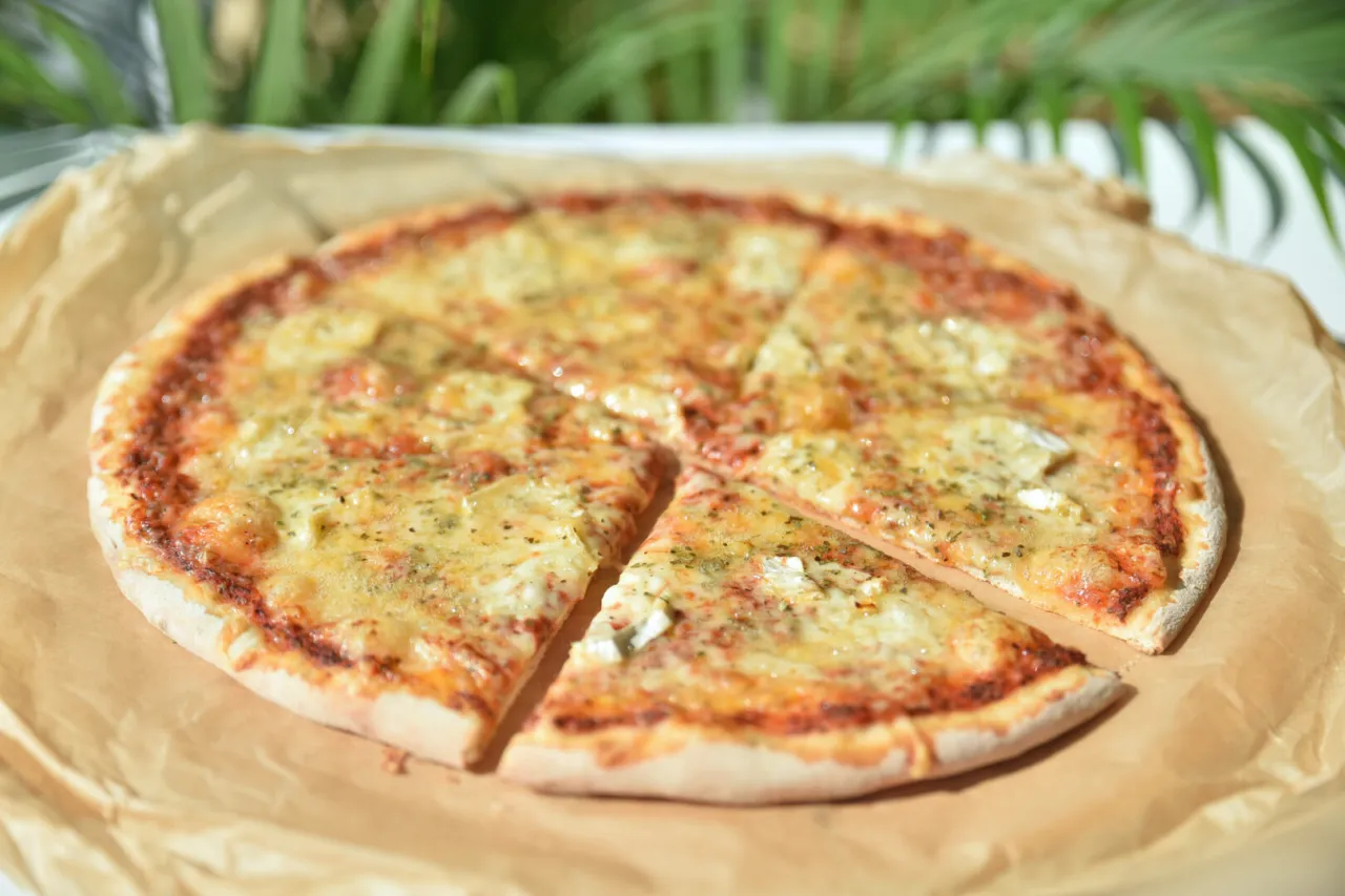 Pyszna pizza z roztopionym, ciągnącym się serem, podana na papierze. Idealna na letnie popołudnie.