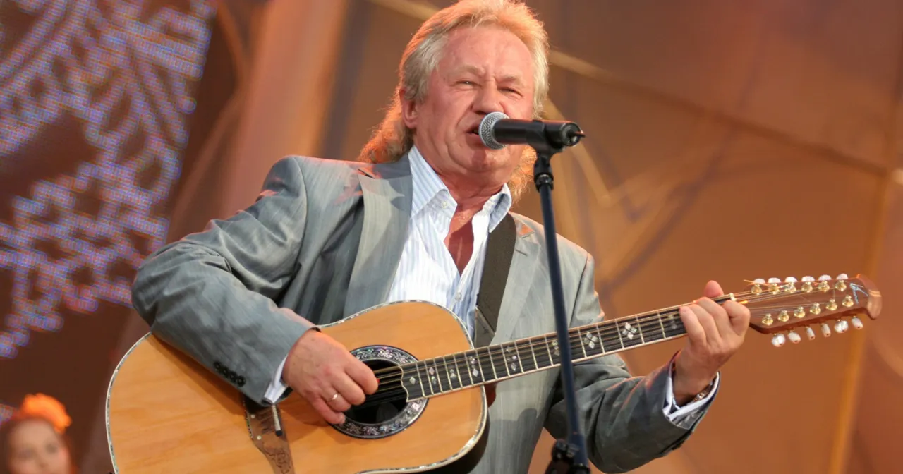 Artysta w szarym garniturze gra na gitarze, śpiewając do mikrofonu. Kto pierwszy śpiewał kolorowe jarmarki?