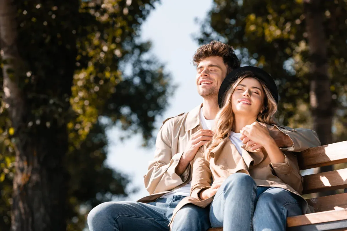 Para siedząca na ławce w parku, ciesząca się słońcem. Ich uśmiechy i bliskość świadczą o trwałych związkach.