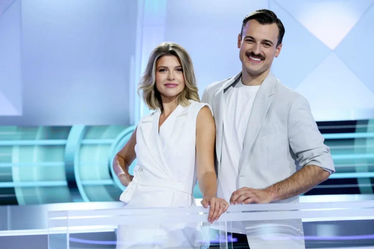 Kto w nowym sezonie będzie prowadził Koło Fortuny? Uśmiechnięci prowadzący w białych strojach na tle studia.