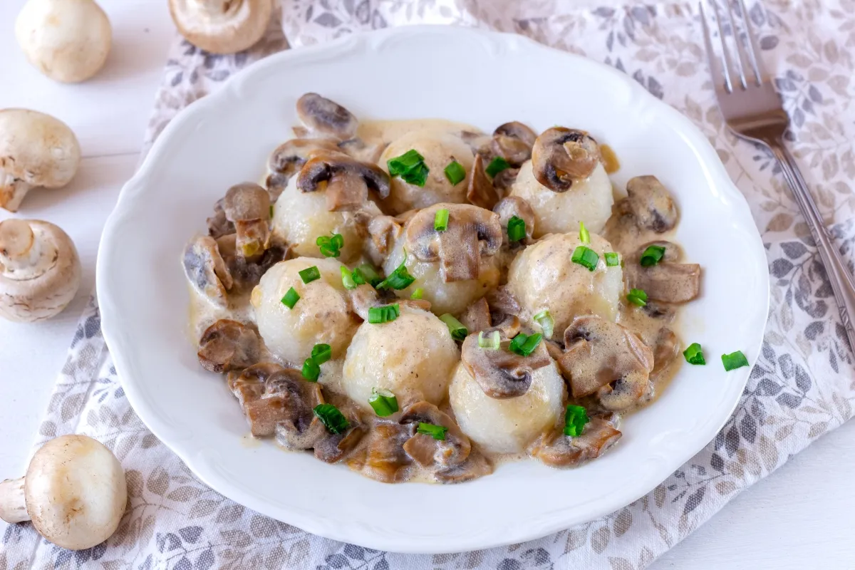 Kluski śląskie w kremowym sosie pieczarkowym, posypane szczypiorkiem. Idealny dodatek do sosu pieczarkowego, który wzbogaci smak.