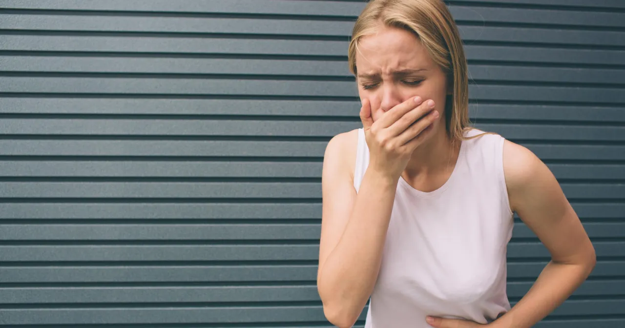 Kobieta z objawami zatrucia, zasłaniająca usta. Jak rozpoznać metanol w domowej wódce i uniknąć zafałszowania alkoholu.