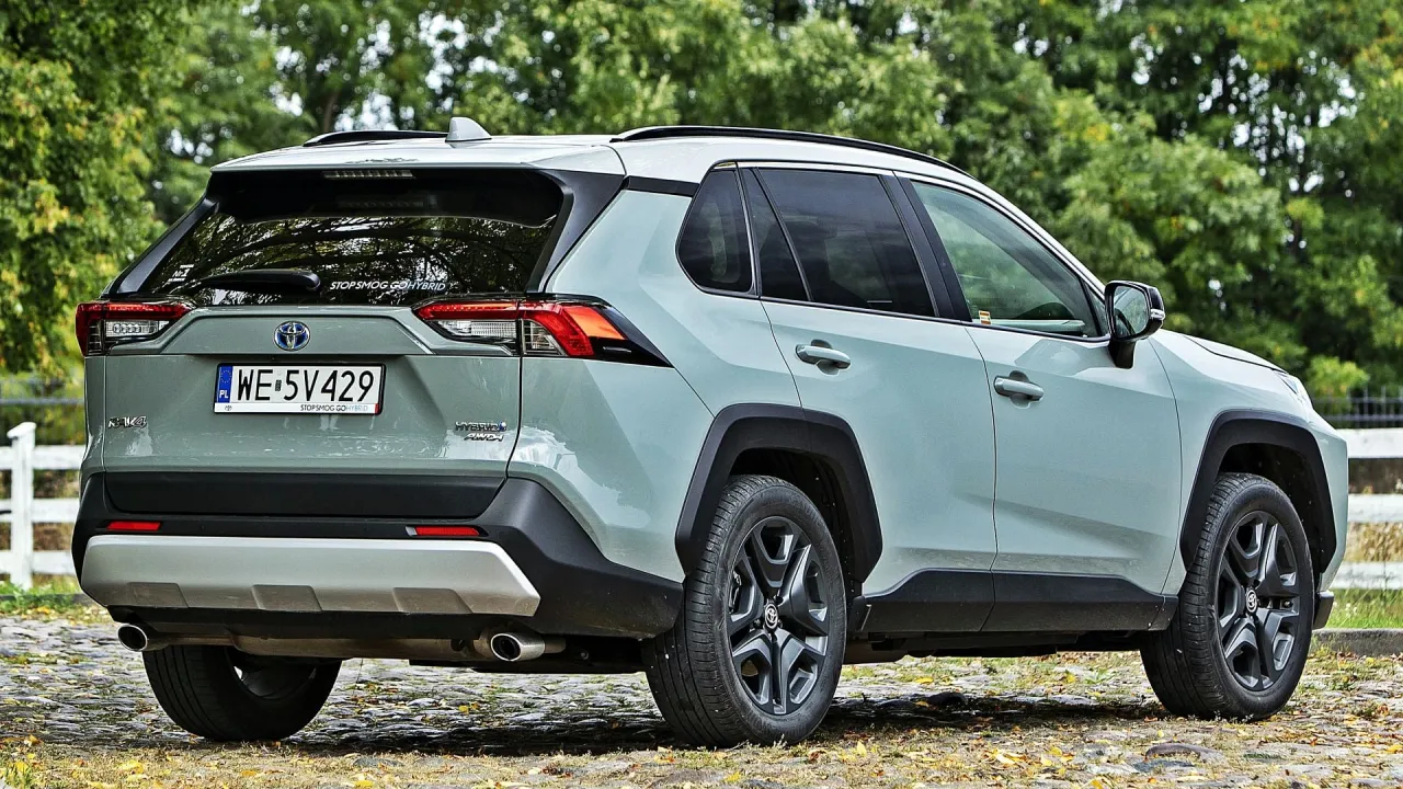Szary SUV Toyota RAV4 Hybrid AWD na tle zieleni. Zastanawiasz się, ile kosztuje Toyota? Ten model to świetny wyb&oacute;r.