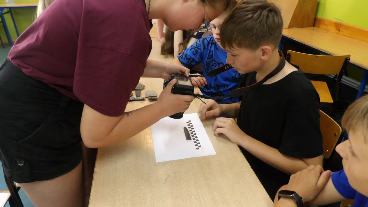 Młodzi pasjonaci uczą się, jak zostać archeologiem, dokumentując znaleziska aparatem.