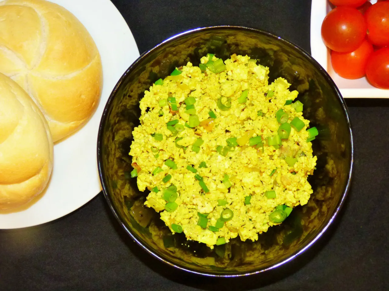 Jajecznica z tofu, zielona cebulka, bułki i pomidorki. Świetny spos&oacute;b, czym zastąpić jajka w diecie wegańskiej.