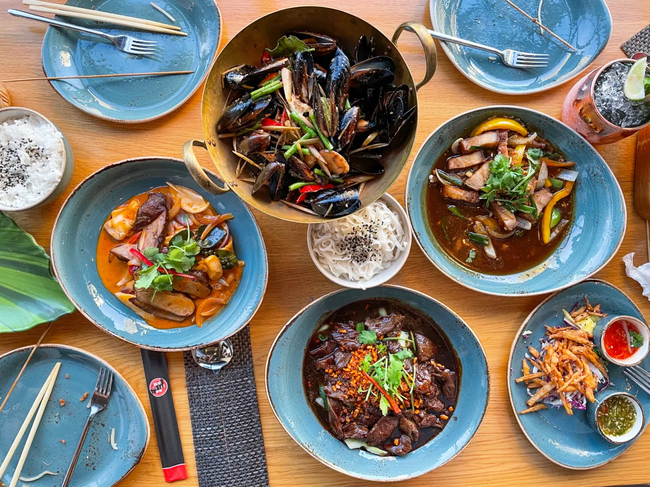 Bogactwo tajskiego jedzenia: małże, wołowina, ryż i inne pyszności na drewnianym stole.
