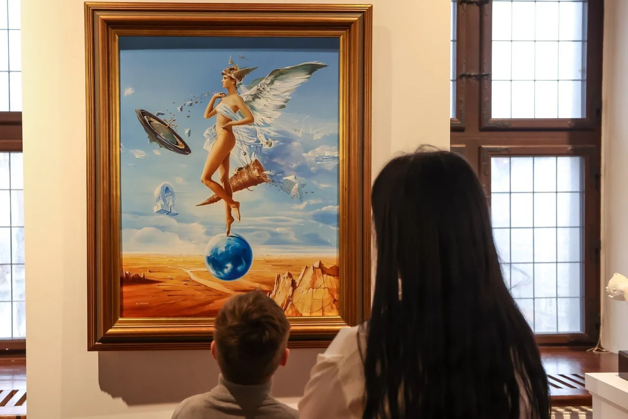 Dzieci podziwiają obraz w muzeum sztuki fantastycznej: skrzydlata postać na kuli ziemskiej, latający dysk i surrealistyczny krajobraz.