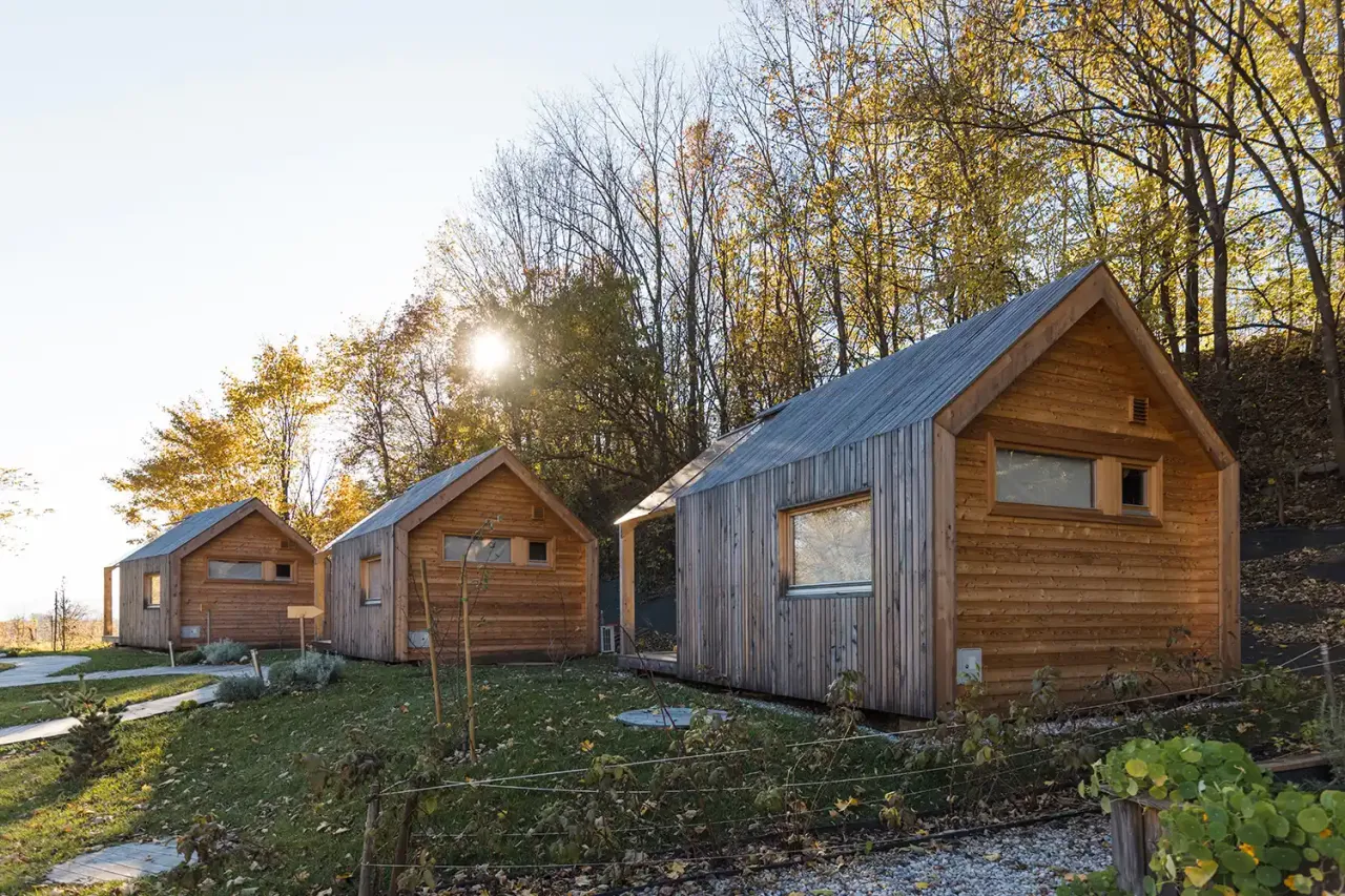 Trzy drewniane domki w jesiennym otoczeniu. Zastanawiasz się, ile potrzeba drewna na dom szkieletowy 100m2?