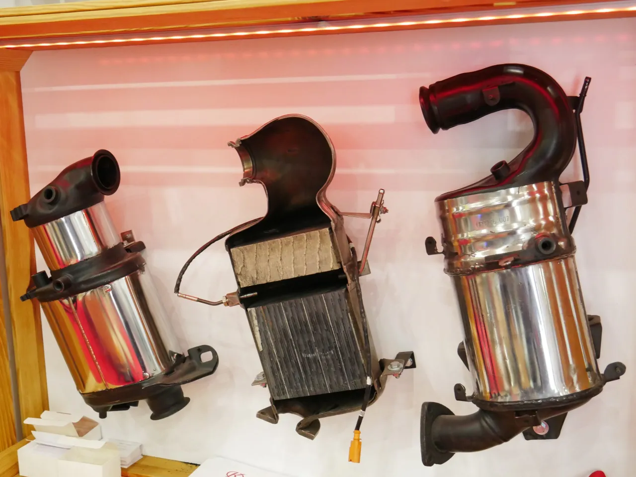 Trzy katalizatory samochodowe, jeden rozcięty, pokazują, do czego służy katalizator: oczyszczanie spalin.