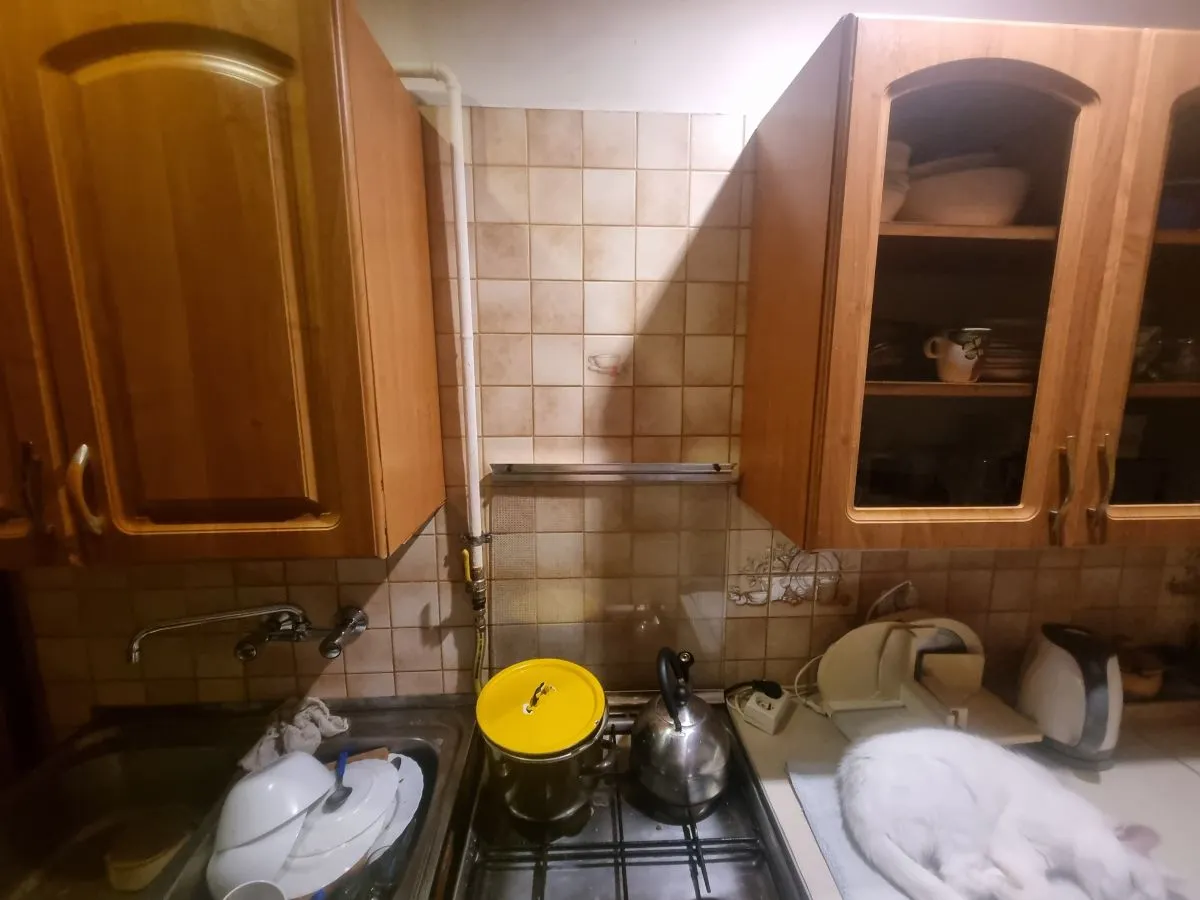 Widok kuchni z zabudową rur gazowych, zlewem, czajnikiem i śpiącym kotem.