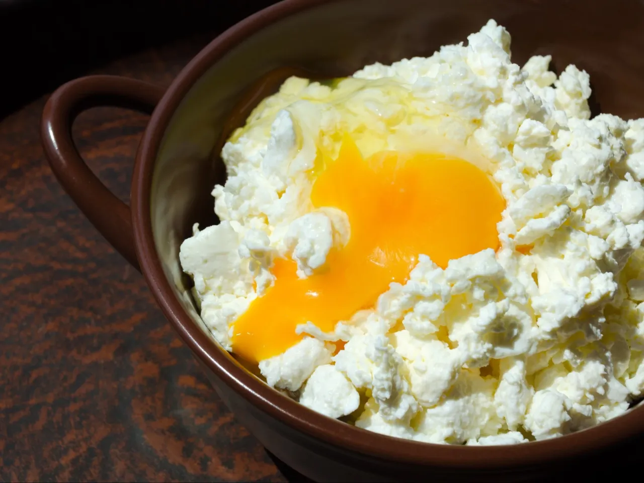 Twaróg z jajkiem w brązowej miseczce. Prosty pomysł na to, co można zrobić z twarogu na obiad.