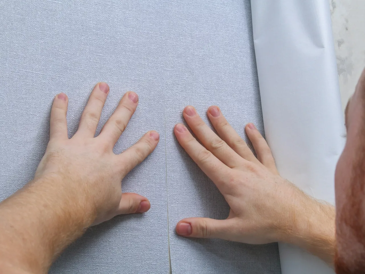 Dłonie sprawdzają fakturę ściany, czy ściana pod tapetę musi być gładka, by dobrze przylegała.