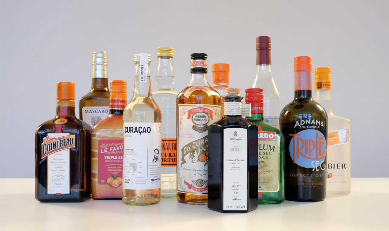 Różne butelki likierów pomarańczowych, w tym Cointreau i inne Triple Sec, gotowe do koktajli.
