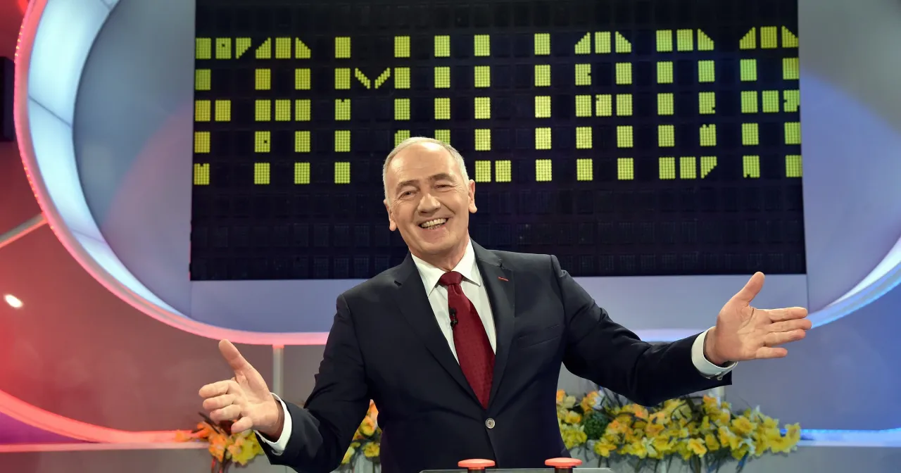 Uśmiechnięty mężczyzna w garniturze, kt&oacute;ry prowadzi Familiadę, gestykuluje radośnie.